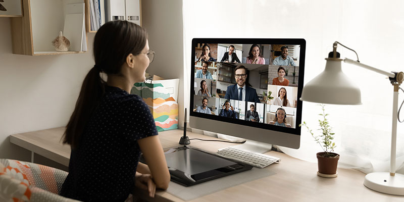 A rear view of a female remote employee holding an online video call with diverse colleagues illustrates remote employee monitoring.